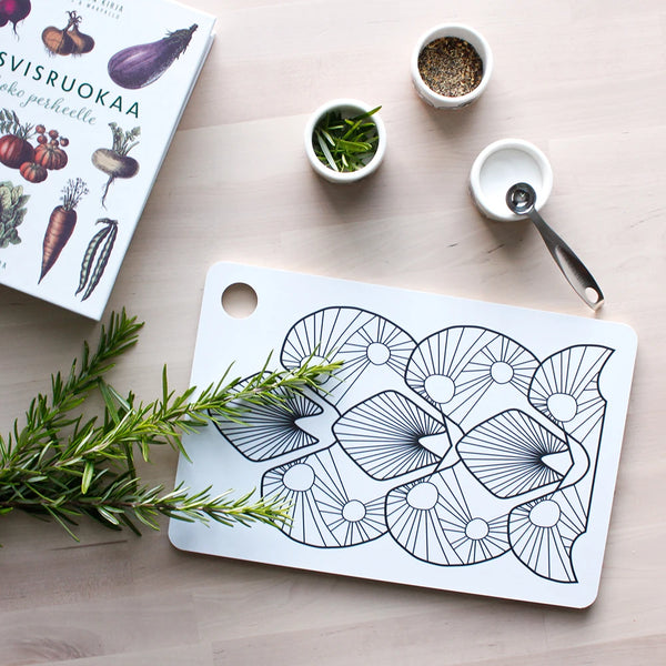 Yläperspektiivistä kuvattu leikkuulauta ja kolme pala-minikuppia sekä keittokirja ja rosmariinin oksa. Leikkuulaudassa on Helmi kuosi mustavalkoisena. Minikupeissa on mausteita ja yhteen kuppiin nojaa rosterinen maustemitta.